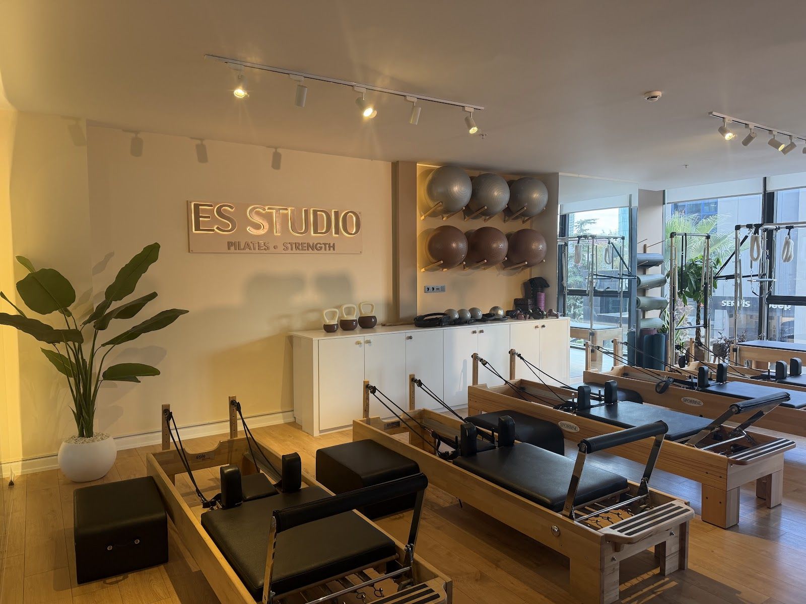 ES Studio reformer salonu: ahşap reformer aletleri, ışıklı ES Studio tabelası ve pilates topları